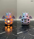 Side by side view of a 3D printed pastel dragon tealight holder showing it lit with a warm glow and unlit on a dark marble surface